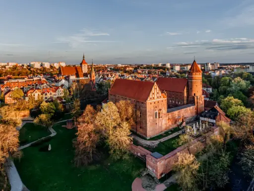 Zachód słońca nad zamkami na Mazurach. Czerwone dachy i ceglane mury w blasku złotej godziny.