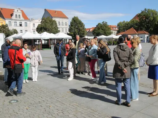 Grupa turystów słucha przewodnika na rynku w Chełmnie, poznając lokalną trasę.