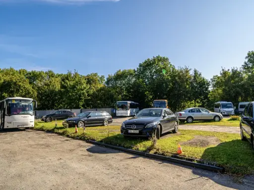 Na parkingu przy zamku Bolków stoi kilka samochodów i autobusów.