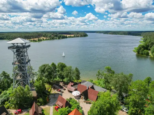 Wieża widokowa nad jeziorem, w tle las i żaglówka. Wdzydze Kiszewskie zapraszają do podziwiania piękna natury.