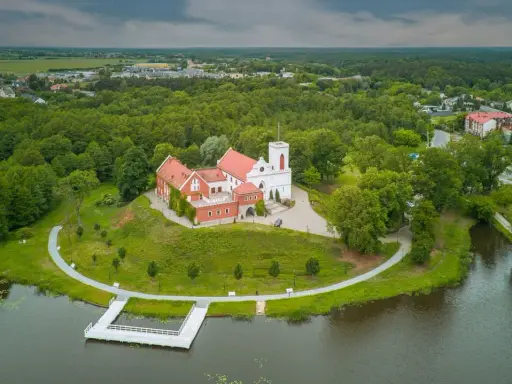 Zamek w Gostyninie, perła pojezierza gostynińsko-włocławskiego, wznosi się nad jeziorem, otoczony zielenią.