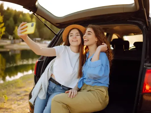 Dwie przyjaciółki robią sobie selfie nad jeziorem, ciesząc się wspólnym weekendem.