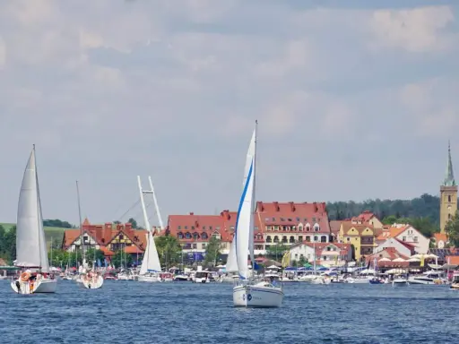 Żaglówki na jeziorze przed malowniczymi mazury miasta z czerwonymi dachami i wieżą kościelną.