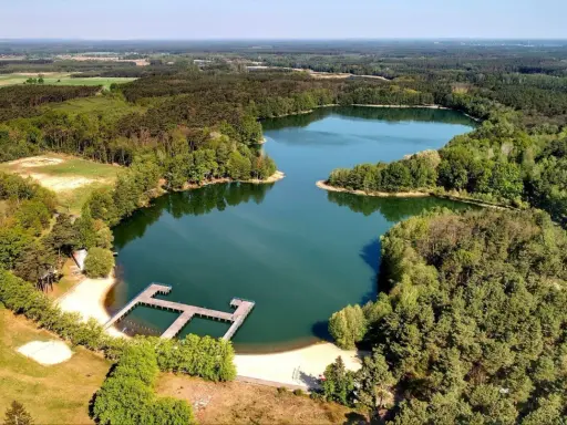 Malownicze jeziora w Zielonej Górze otoczone lasem, z drewnianym pomostem i piaszczystą plażą. Idealne miejsce na wypoczynek.
