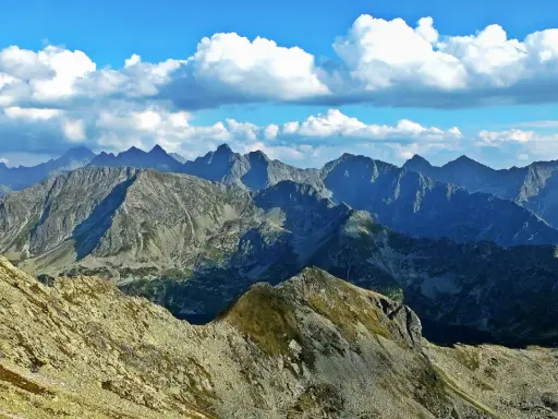 Widok na skaliste pasmo górskie, gdzie każdy zawrat szczyt zapiera dech. Błękitne niebo z białymi chmurami nad ostrymi grzbietami.