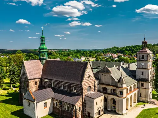 Wąchock atrakcje: Opactwo Cystersów z zieloną wieżą i wieżą zegarową na tle błękitnego nieba z chmurami.