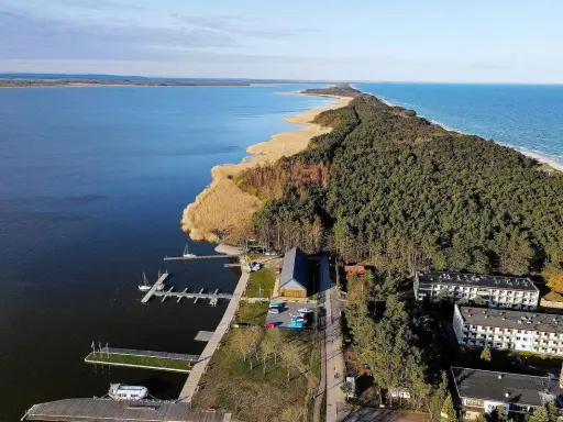 Dąbki atrakcje: malowniczy widok na jezioro, las, plażę i budynki. Widoczne molo, przystań jachtowa i zabudowania.