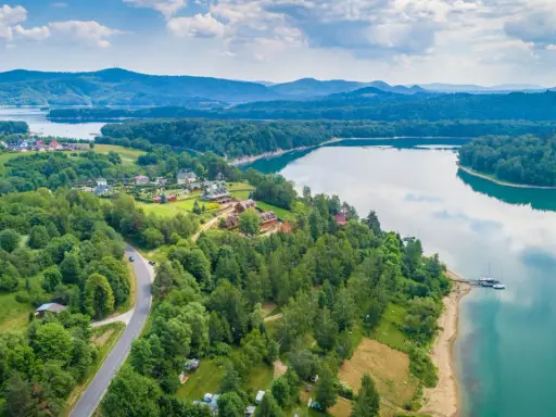 Malownicze jezioro podkarpackie otoczone lasami, z widokiem na domki letniskowe i góry w oddali.