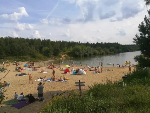 Tłoczna plaża nad jeziorem trzciańskim. Ludzie opalają się, kąpią i odpoczywają na piasku.