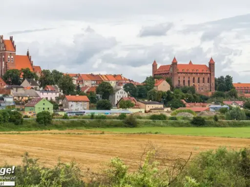 Widok na miasteczko z ceglanymi zamkami i kościołami, otoczone zielenią. W oddali pola uprawne. Wspaniałe **atrakcje** czekają na odkrycie!