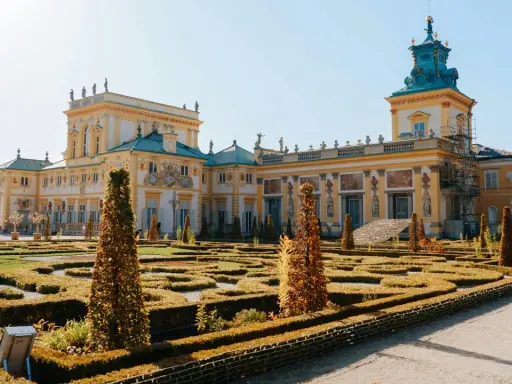 Barokowy pałac z żółtą fasadą i zielonym dachem, otoczony geometrycznym ogrodem. Wnętrze pałacu zachwyca bogactwem zdobień.