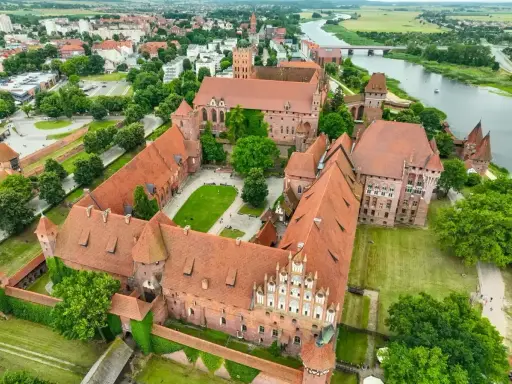 Malbork, największy zamek w Polsce, rozciąga się wzdłuż rzeki Nogat. Jego ceglane mury i liczne wieże tworzą imponujący krajobraz.