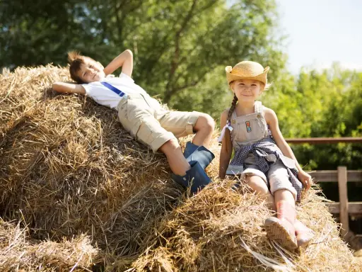 Dzieci odpoczywają na sianie podczas wakacji na agroturystyce dla dzieci ze zwierzętami.