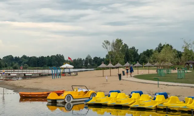 Plaża z żółtymi rowerami wodnymi i łódkami, idealna na weekendowy wypad na Mazury blisko Warszawy.