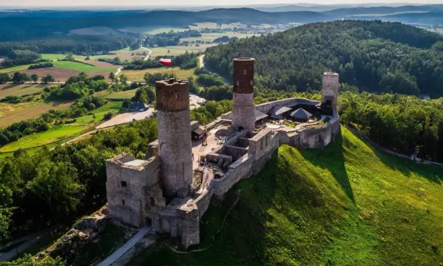 Zamek w Górach Świętokrzyskich, majestatycznie wznoszący się na wzgórzu, otoczony zielenią i malowniczym krajobrazem.