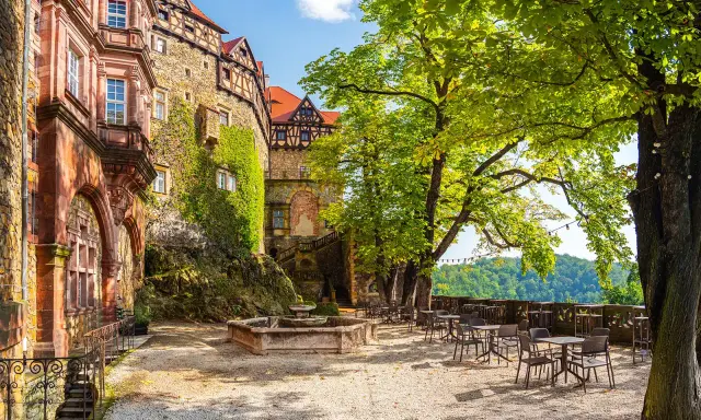 Zamek Książ z tarasami i fontanną, otoczony zielenią, zaprasza do odpoczynku.