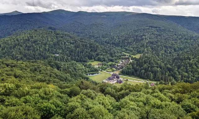 Widok z tarasu widokowego Bieszczady na zieloną dolinę z jeziorem i zabudowaniami.