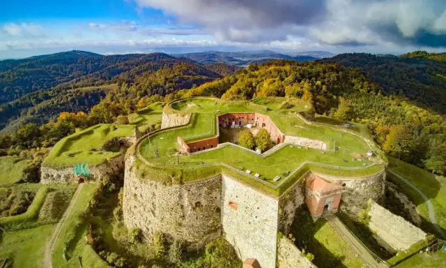 Twierdza w kształcie gwiazdy na wzgórzu, otoczona jesiennymi lasami. To malowniczy wschód Polski, gdzie historia spotyka się z naturą.