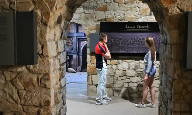 Zwiedzający podziwiają fragment nagrobka "Lament Opatowski" w kamiennych murach.