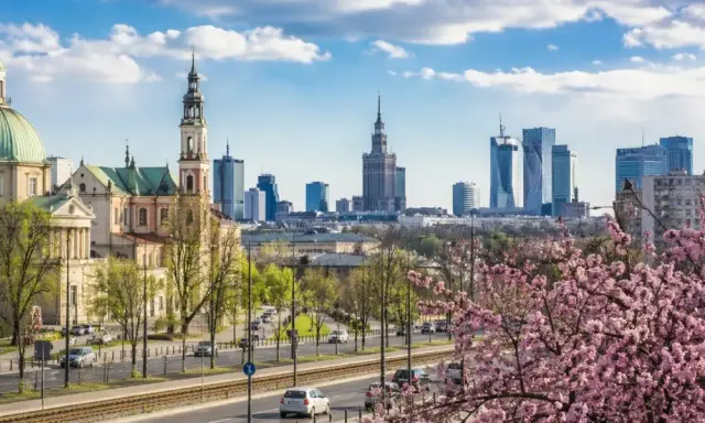 Majówka w Warszawie: zabytkowy kościół i nowoczesne wieżowce na tle kwitnącej wiśni.