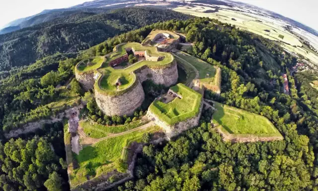 Forteca na wzgórzu, otoczona lasem, z widokiem na pola. Idealne miejsce na odkrywanie podziemnych tras turystycznych.