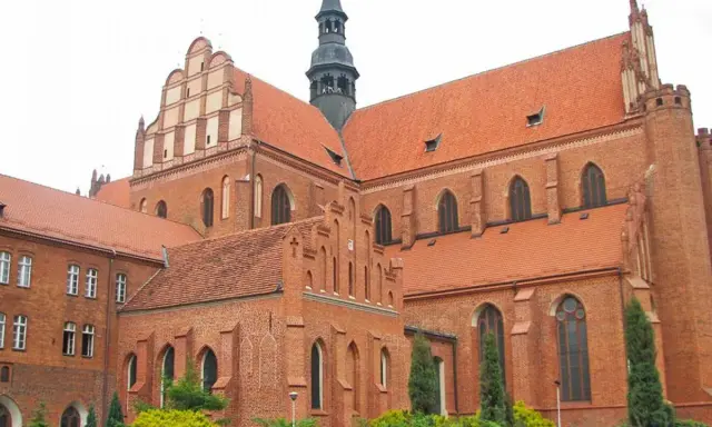 Majestatyczna pelplińska katedra z cegły, z charakterystycznymi dachami i wieżą, góruje nad otoczeniem.