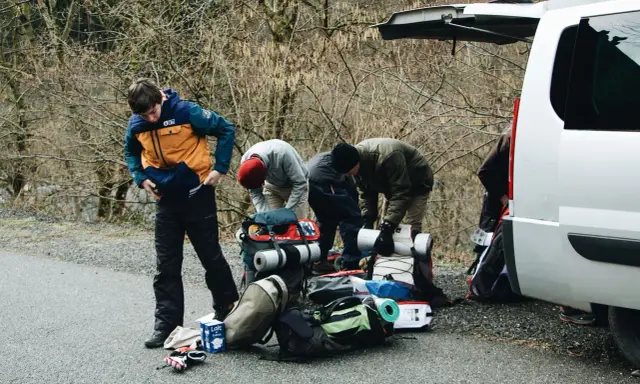 Grupa ludzi przygotowuje sprzęt do wyprawy w **Tatry Wysokie**. Widać plecaki, karimaty i torby przy białym samochodzie.