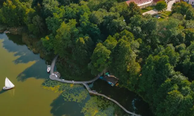 Idealne miejsce, gdzie nad jezioro w Polsce. Drewniana kładka prowadzi do łodzi i żaglówki, otoczone bujną zielenią.