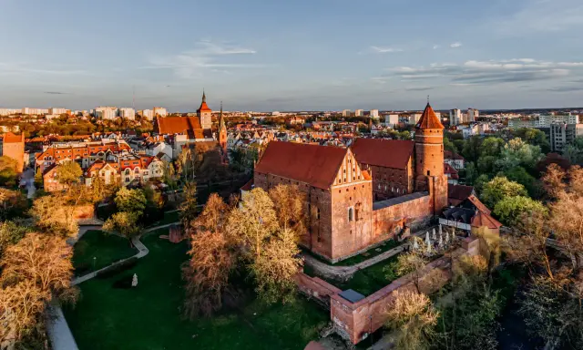 Zachód słońca nad zamkami na Mazurach. Czerwone dachy i ceglane mury w blasku złotej godziny.