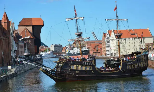 Gdański galeon "Lew" z pasażerami na pokładzie, na tle zabytkowej architektury miasta. To jeden z 7 ciekawych faktów o Polsce, które można odkryć w tym mieście.