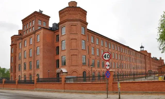 Imponujący ceglany budynek dawnego Księży Młyn, idealny na zwiedzanie. Widać znaki drogowe i ogrodzenie.