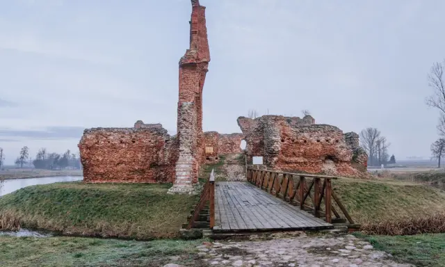 Ruiny zamku w okolicach Łodzi tak do 100 km. Drewniany mostek prowadzi do ceglanych murów.