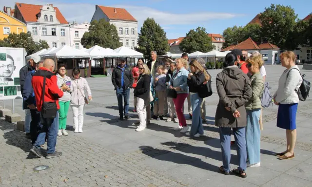 Grupa turystów słucha przewodnika na rynku w Chełmnie, poznając lokalną trasę.