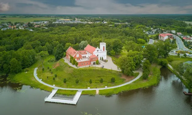 Zamek w Gostyninie, perła pojezierza gostynińsko-włocławskiego, wznosi się nad jeziorem, otoczony zielenią.