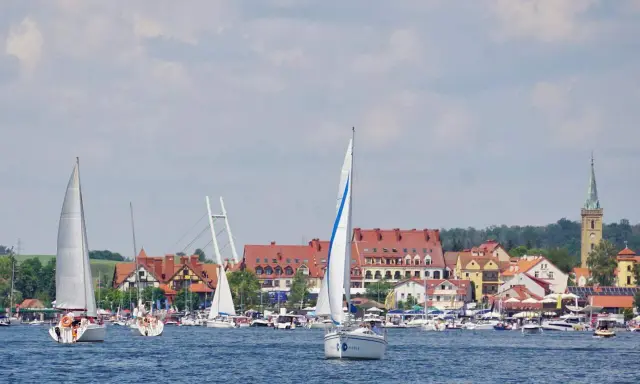 Żaglówki na jeziorze przed malowniczymi mazury miasta z czerwonymi dachami i wieżą kościelną.