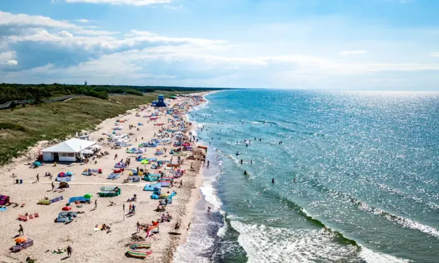 Tłum ludzi na plaży w Darłowie, korzystających z uroków lata. Wiele kolorowych parawanów i namiotów, a w wodzie kąpielowicze. To idealne darłowo atrakcje dla każdego.