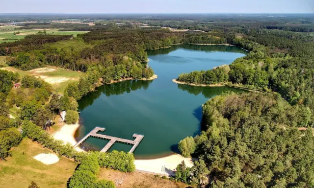 Malownicze jeziora w Zielonej Górze otoczone lasem, z drewnianym pomostem i piaszczystą plażą. Idealne miejsce na wypoczynek.