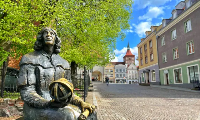 Pomnik Kopernika, jedna z głównych atrakcji Olsztyna, na tle kolorowych kamienic i błękitnego nieba.