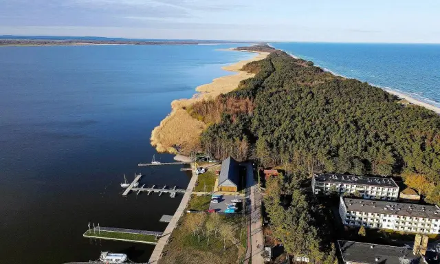 Dąbki atrakcje: malowniczy widok na jezioro, las, plażę i budynki. Widoczne molo, przystań jachtowa i zabudowania.