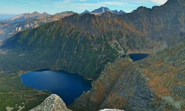 Widok na Tatry z góry. Na pierwszym planie skały, w dole las i jezioro Morskie Oko.