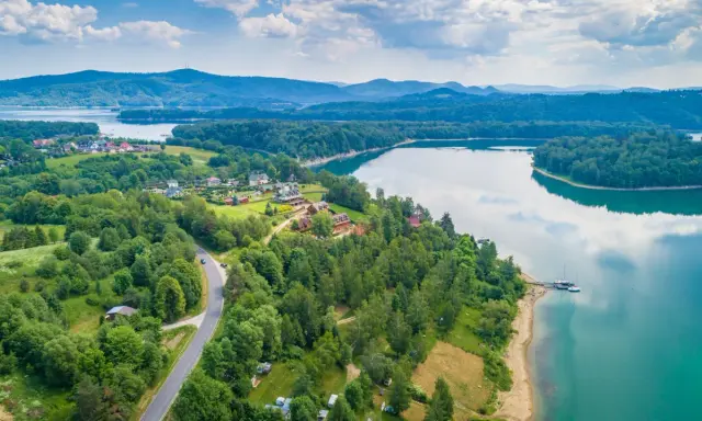 Malownicze jezioro podkarpackie otoczone lasami, z widokiem na domki letniskowe i góry w oddali.