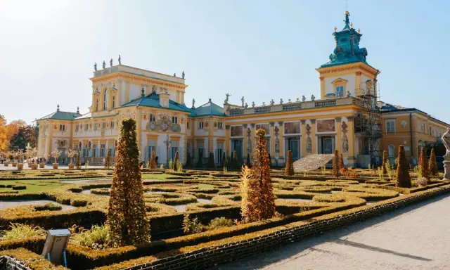 Barokowy pałac z żółtą fasadą i zielonym dachem, otoczony geometrycznym ogrodem. Wnętrze pałacu zachwyca bogactwem zdobień.