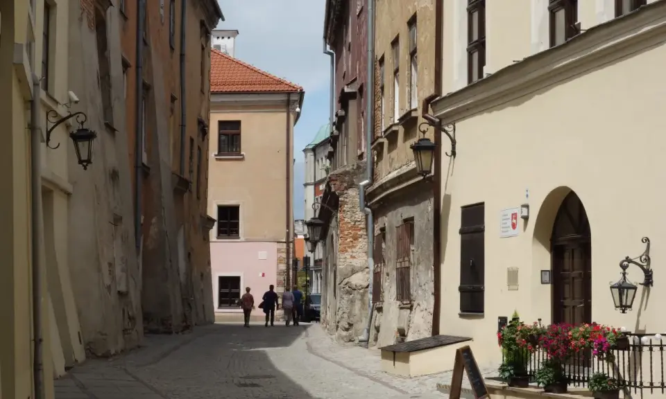 Wąska, brukowana uliczka w Lublinie z kamienicami i kilkoma spacerującymi osobami.