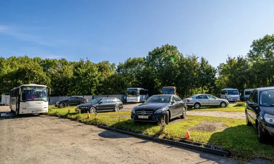 Na parkingu przy zamku Bolków stoi kilka samochodów i autobusów.