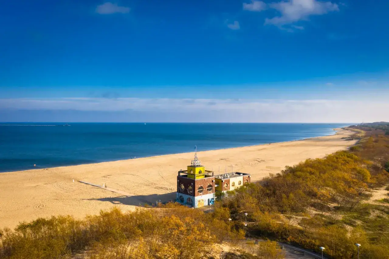Piękna plaża i morze, idealne na spacer po urokliwych **miejscowościach nad morzem koło Gdańska**. W oddali widać charakterystyczny budynek.