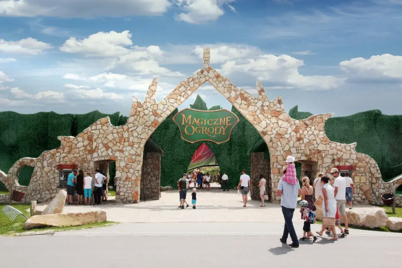 Kamienna brama "Magiczne Ogrody" zaprasza na świetne atrakcje dla nastolatków. Rodziny wchodzą do parku rozrywki.