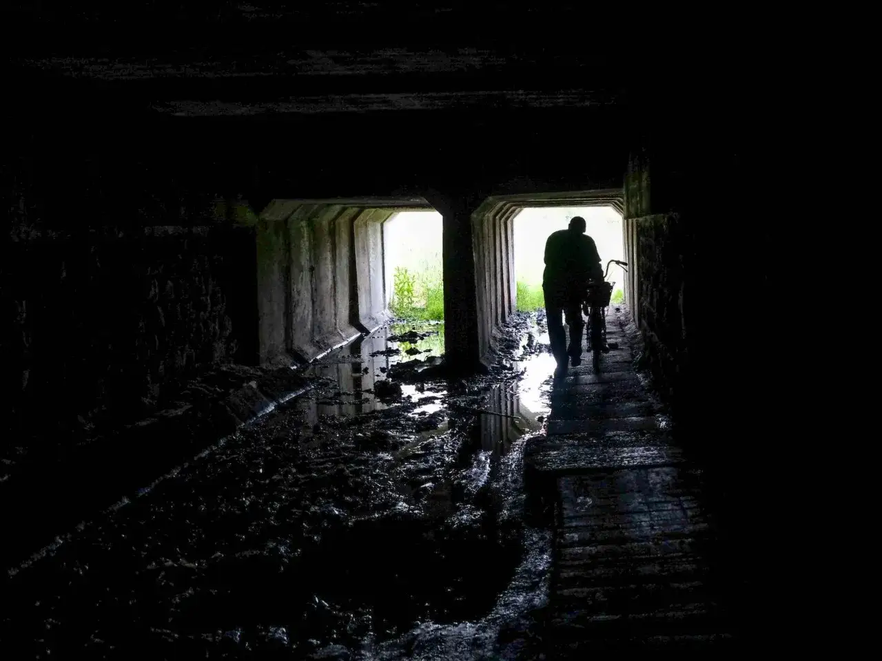 Mroczny tunel, błoto i woda. Postać z rowerem wychodzi w jasność. Czy to początek drogi przez nawiedzone miejsca w Polsce?