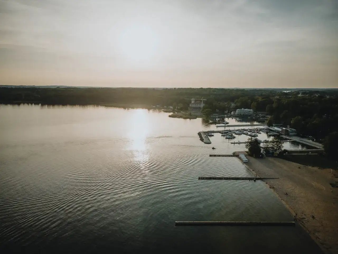 Zachód słońca nad jeziorem w Giżycku. Widok na plażę, przystań z łodziami i las.