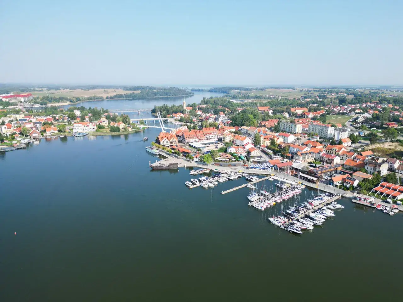 Widok na miasteczko z mariną pełną żaglówek i łodzi. W tle jezioro i most, idealne miejsce na letni wypoczynek, jak na mikołajki na plaży.