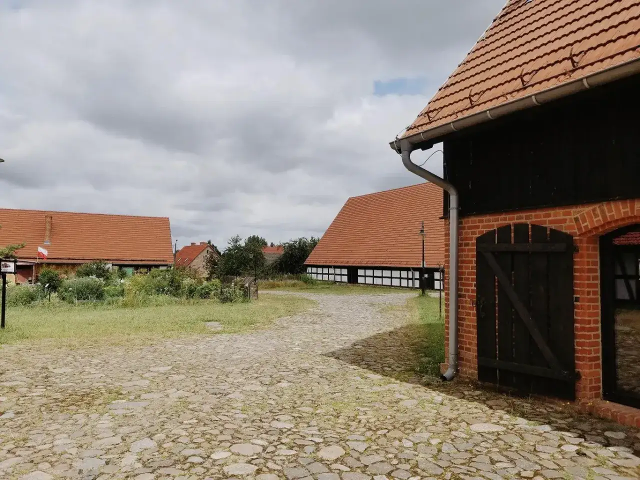 Swołowo skansen: brukowana droga prowadzi do tradycyjnych domów z czerwonymi dachami i drewnianymi elementami.